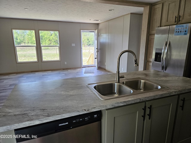 kitchen featuring stainless steel appliances, a sink, a textured ceiling, light wood-type flooring, and light countertops