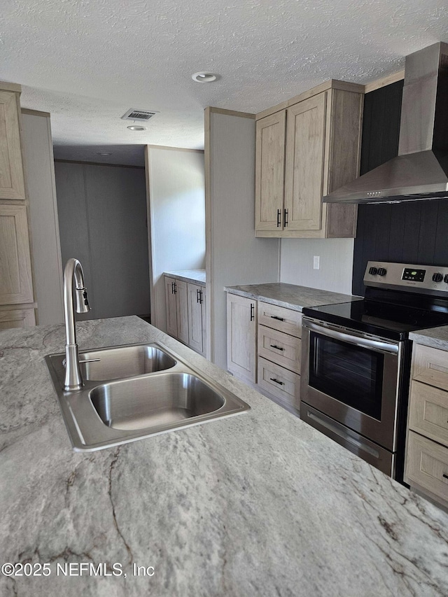 kitchen with light brown cabinetry, visible vents, a sink, wall chimney exhaust hood, and electric range