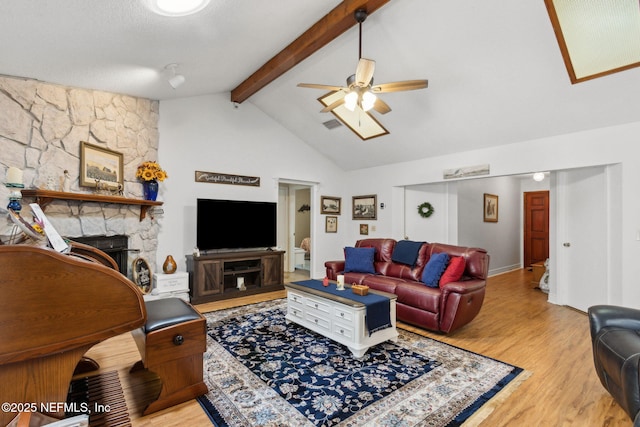 living area featuring beamed ceiling, ceiling fan, a fireplace, wood finished floors, and high vaulted ceiling