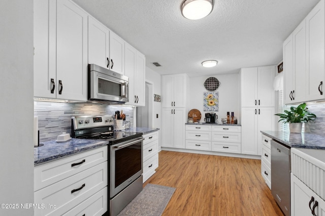 kitchen featuring stainless steel appliances, light wood-style floors, visible vents, backsplash, and a textured ceiling