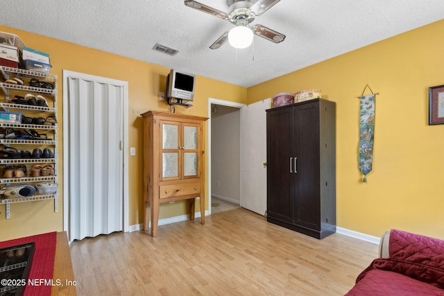 interior space with a ceiling fan, visible vents, light wood-style flooring, and a textured ceiling