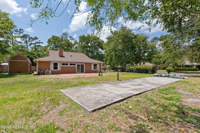 rear view of property with a chimney, a yard, an outbuilding, a patio area, and a shed