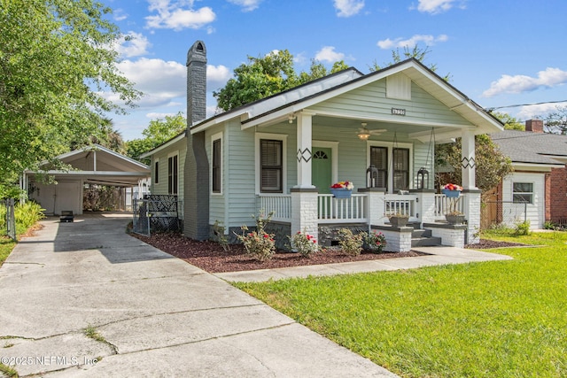bungalow-style home featuring a porch, a front yard, a detached carport, a chimney, and concrete driveway