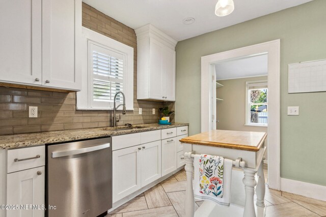 kitchen with white cabinetry, tasteful backsplash, stainless steel dishwasher, a sink, and light stone countertops