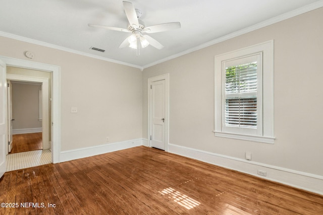 empty room featuring crown molding, a ceiling fan, visible vents, baseboards, and hardwood / wood-style flooring