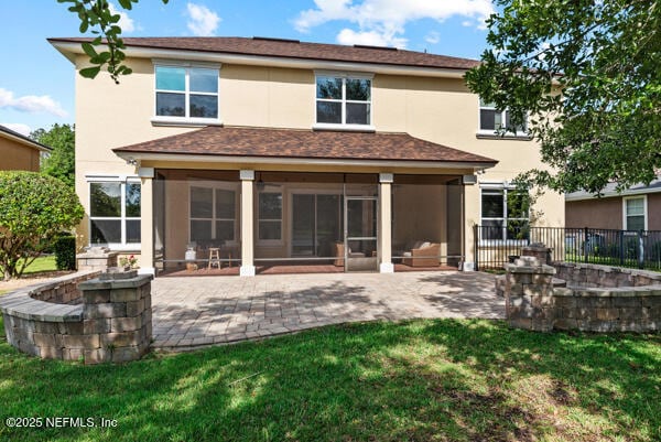 rear view of property featuring a yard, stucco siding, a sunroom, and a patio area