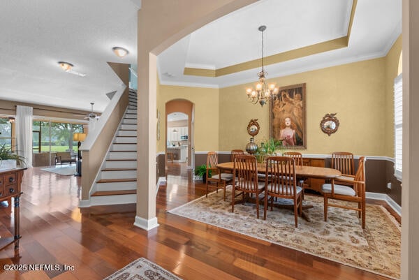 dining space featuring an inviting chandelier, stairway, a tray ceiling, ornamental molding, and arched walkways