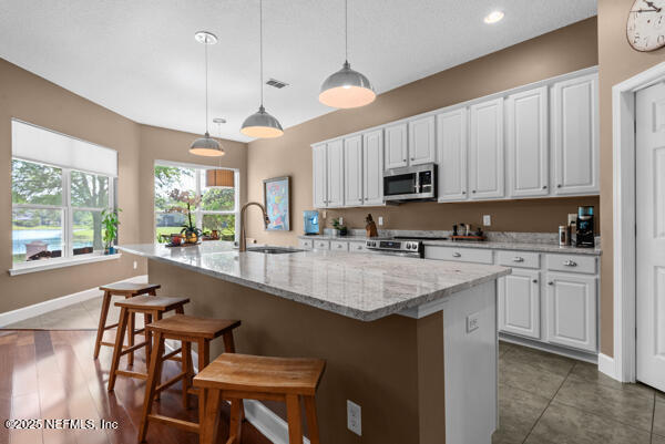 kitchen featuring white cabinets, a sink, stainless steel appliances, baseboards, and a kitchen bar