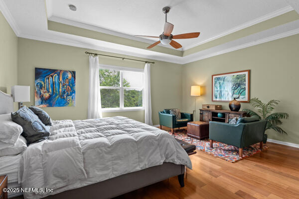 bedroom with crown molding, wood finished floors, a raised ceiling, and baseboards