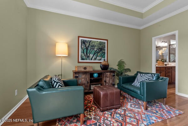 sitting room with crown molding, a raised ceiling, wood finished floors, and baseboards
