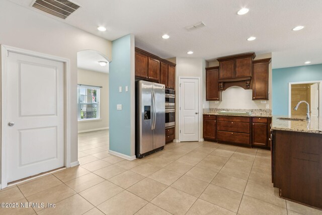 kitchen featuring visible vents, light stone countertops, arched walkways, a sink, and appliances with stainless steel finishes
