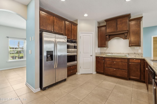 kitchen featuring arched walkways, light tile patterned floors, light stone counters, stainless steel appliances, and recessed lighting