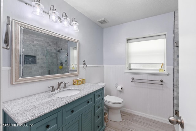 bathroom featuring wainscoting, a shower stall, toilet, vanity, and visible vents