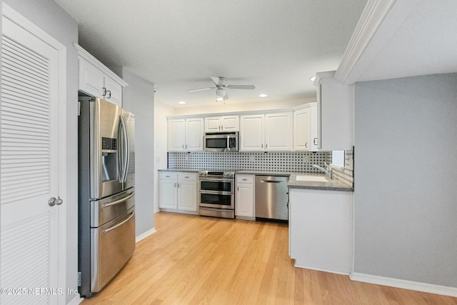 kitchen with a sink, stainless steel appliances, decorative backsplash, a ceiling fan, and white cabinets