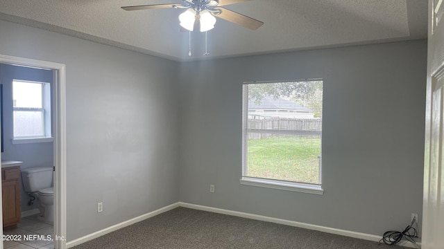 empty room with a textured ceiling, ceiling fan, light colored carpet, and baseboards