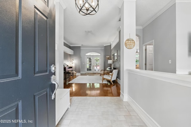 foyer entrance with ornamental molding, arched walkways, french doors, baseboards, and a notable chandelier