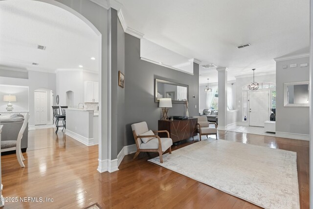 entryway featuring visible vents, ornamental molding, arched walkways, light wood-type flooring, and baseboards