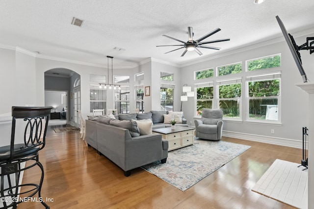 living area with arched walkways, a ceiling fan, wood finished floors, and a wealth of natural light