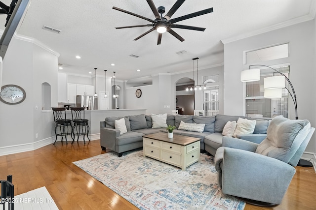 living area featuring arched walkways, crown molding, visible vents, and ceiling fan with notable chandelier