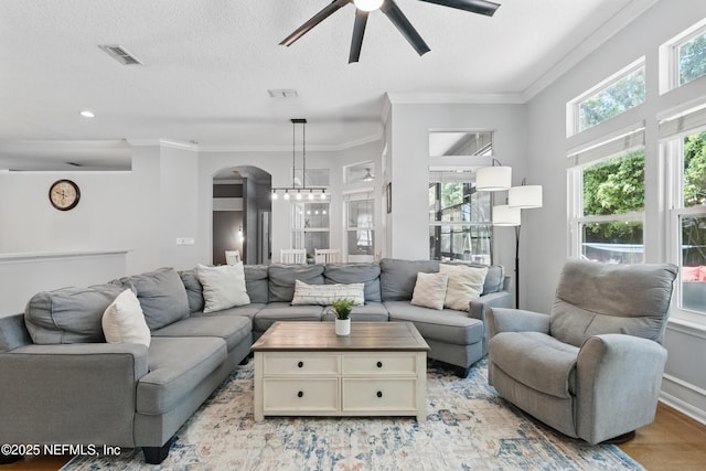 living room with a ceiling fan, visible vents, arched walkways, and crown molding