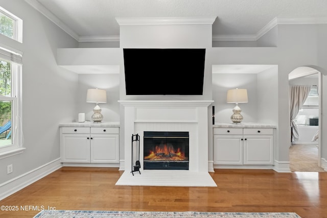 unfurnished living room with arched walkways, ornamental molding, a brick fireplace, and light wood-type flooring