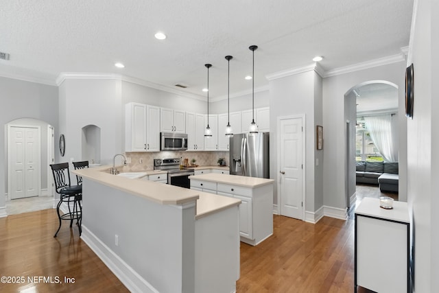 kitchen with stainless steel appliances, a peninsula, arched walkways, baseboards, and a kitchen island