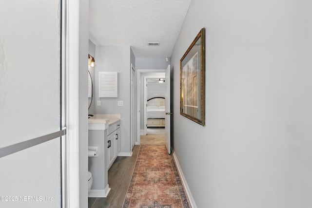hallway featuring wood finished floors, a textured ceiling, baseboards, and visible vents