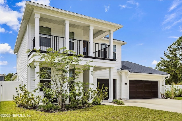 greek revival house featuring a garage, concrete driveway, a balcony, and fence