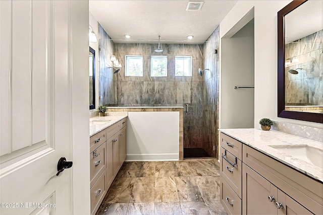 full bathroom featuring a shower stall, two vanities, a sink, and visible vents