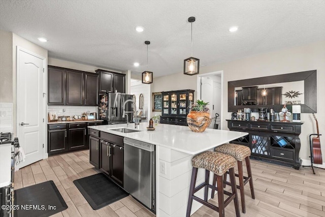 kitchen with tasteful backsplash, a sink, stainless steel appliances, light countertops, and wood finish floors