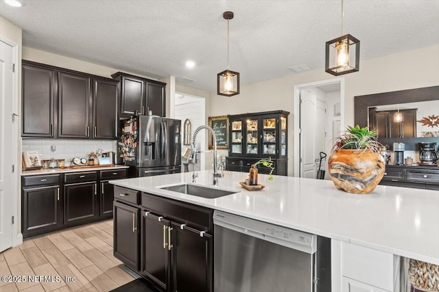 kitchen with a sink, pendant lighting, stainless steel appliances, light countertops, and backsplash