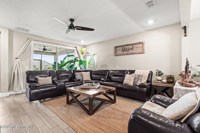 living room with light wood-type flooring, visible vents, a textured ceiling, and ceiling fan