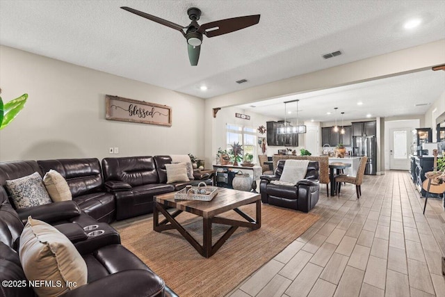 living area featuring light wood finished floors, visible vents, a textured ceiling, and ceiling fan