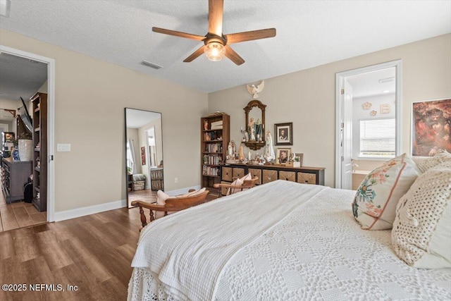 bedroom with wood finished floors, ensuite bathroom, a walk in closet, baseboards, and visible vents