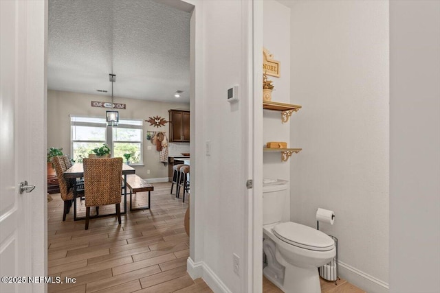 bathroom with wood finished floors, baseboards, a textured ceiling, and toilet