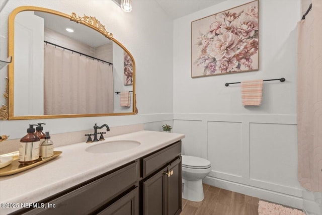 bathroom with curtained shower, a wainscoted wall, toilet, vanity, and a decorative wall