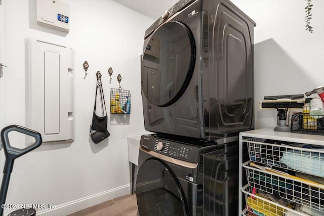 clothes washing area with wood finished floors, baseboards, stacked washing maching and dryer, and laundry area
