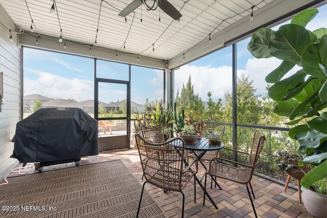 sunroom / solarium featuring brick floor, outdoor dining area, and ceiling fan