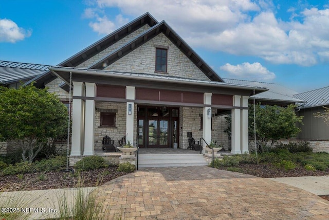 view of front of house featuring a standing seam roof, stone siding, and covered porch