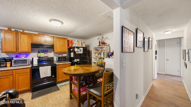 kitchen featuring brown cabinetry, visible vents, under cabinet range hood, light wood finished floors, and black appliances