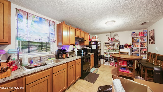 kitchen featuring light countertops, a textured ceiling, under cabinet range hood, visible vents, and black appliances