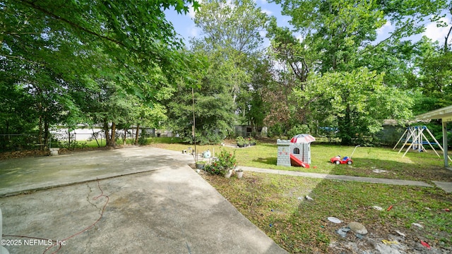 view of yard featuring a playground, a patio, concrete driveway, and a fenced backyard
