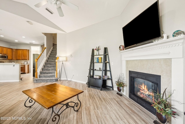 living room featuring light wood finished floors, visible vents, lofted ceiling, a ceiling fan, and a fireplace