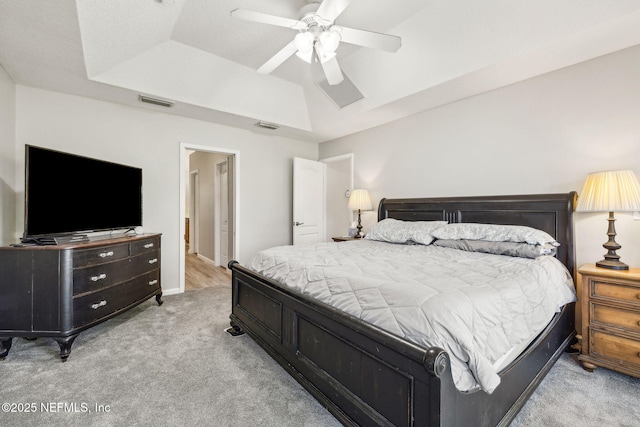 bedroom with a raised ceiling, visible vents, light colored carpet, and ceiling fan