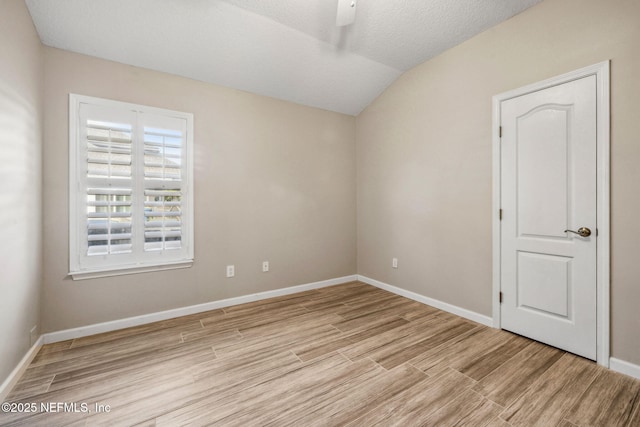 spare room featuring wood finished floors, vaulted ceiling, baseboards, and a textured ceiling