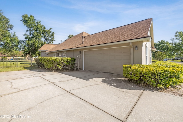view of front of home featuring roof with shingles, driveway, fence, a garage, and stucco siding