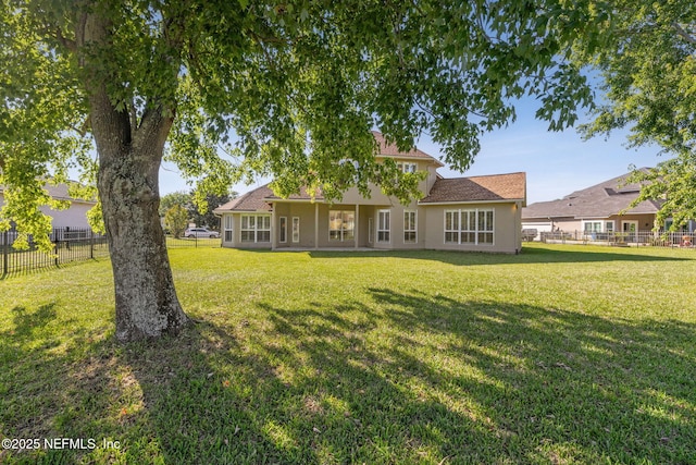 rear view of property featuring fence, a lawn, and stucco siding