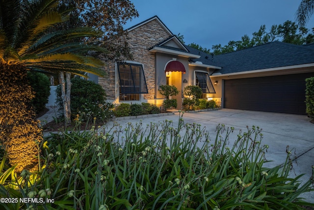 view of front of house with stucco siding, driveway, stone siding, and a garage