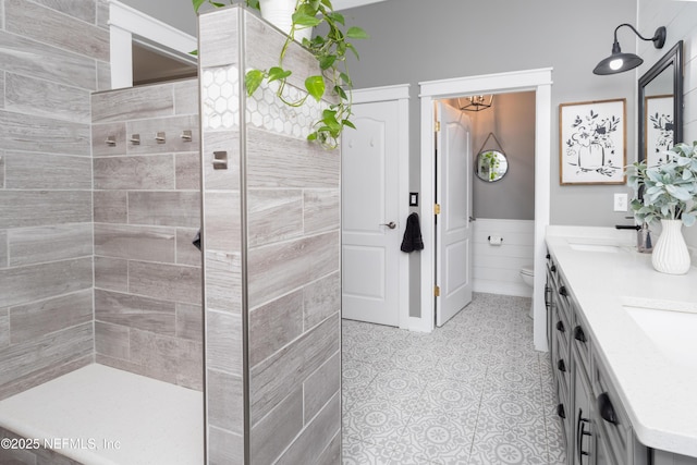 bathroom with a sink, wainscoting, walk in shower, double vanity, and toilet