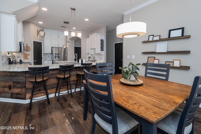dining space featuring dark wood finished floors, arched walkways, ornamental molding, and recessed lighting